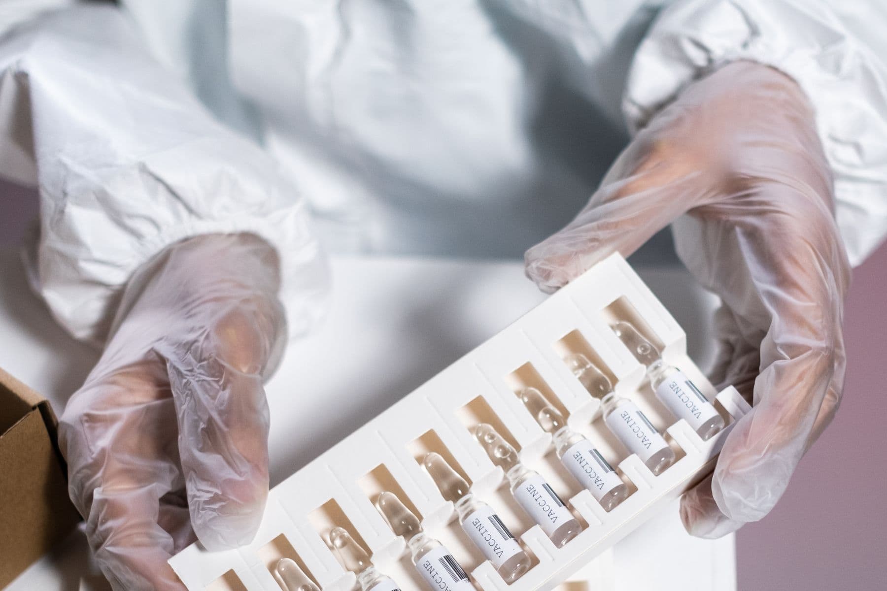 Gloved hands packing a tray of labelled pharmaceutical vials into a carton